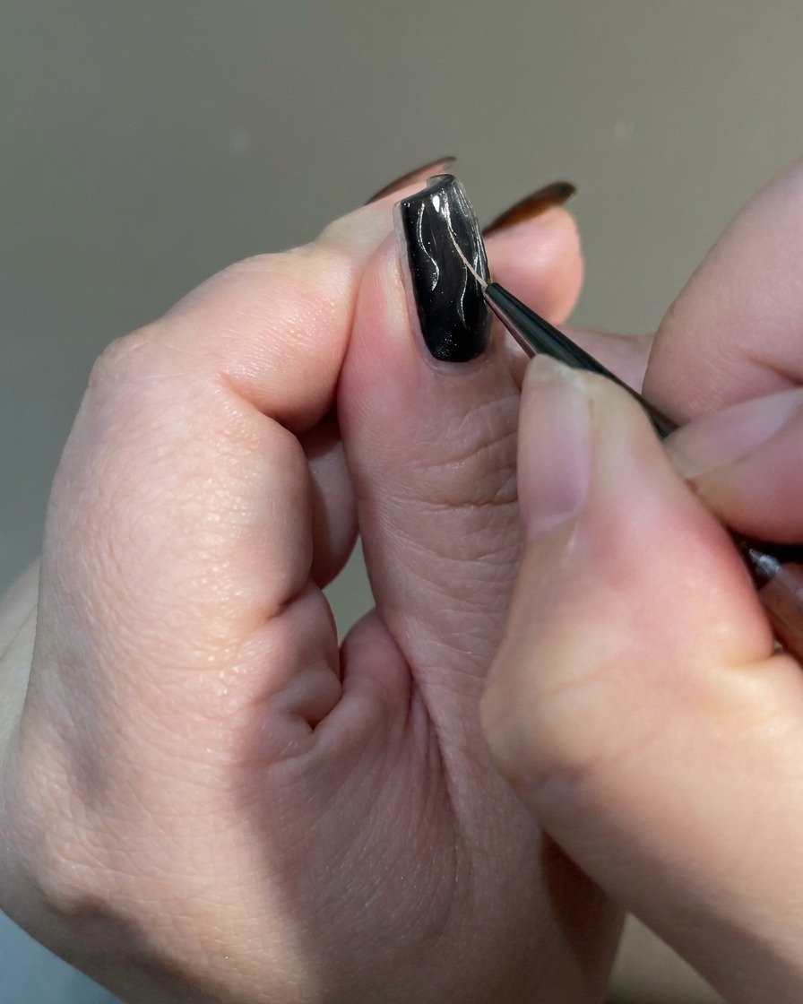 Un gros plan dun pinceau fin effilant les extrémités des motifs de flamme sur un ongle pour créer une finition pointue et irrégulière.