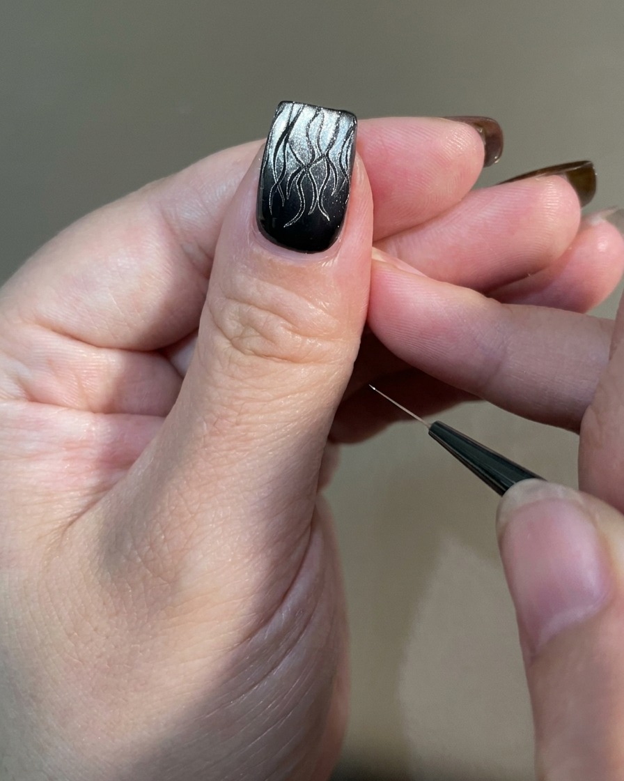 Une main avec un nail art de flamme terminé placée sous une lampe UV professionnelle.