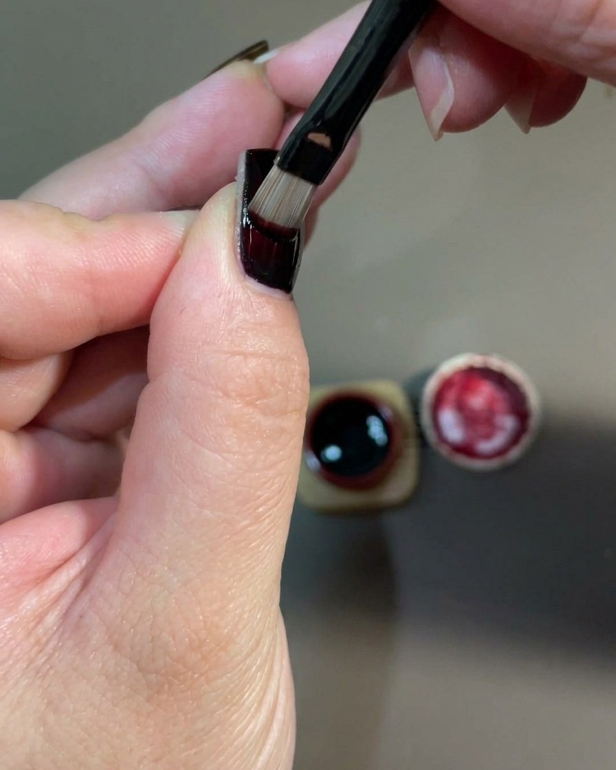 Un gros plan dune main placée dans une lampe UV pour catalyser la couche de gel rouge fraîchement appliquée.