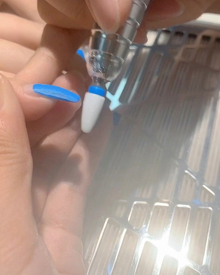 Gros plan dun embout de ponceuse retirant du gel bleu sur un ongle naturel.