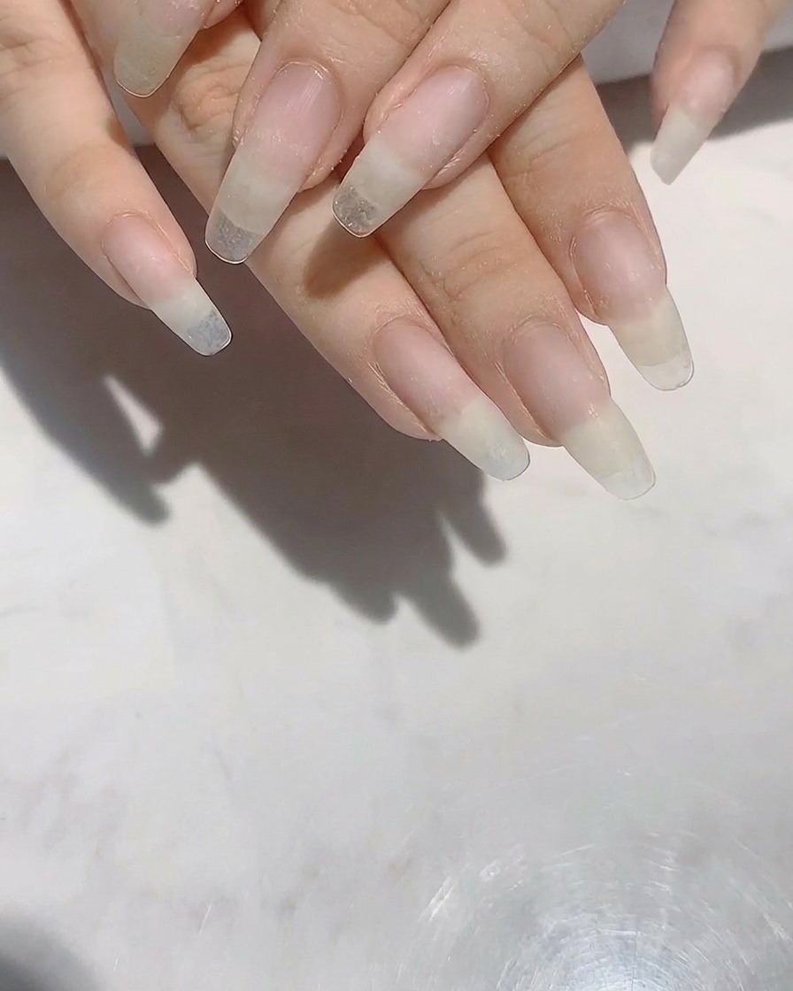 Mains avec de longs ongles naturels en cours de limage pour perfectionner la forme.