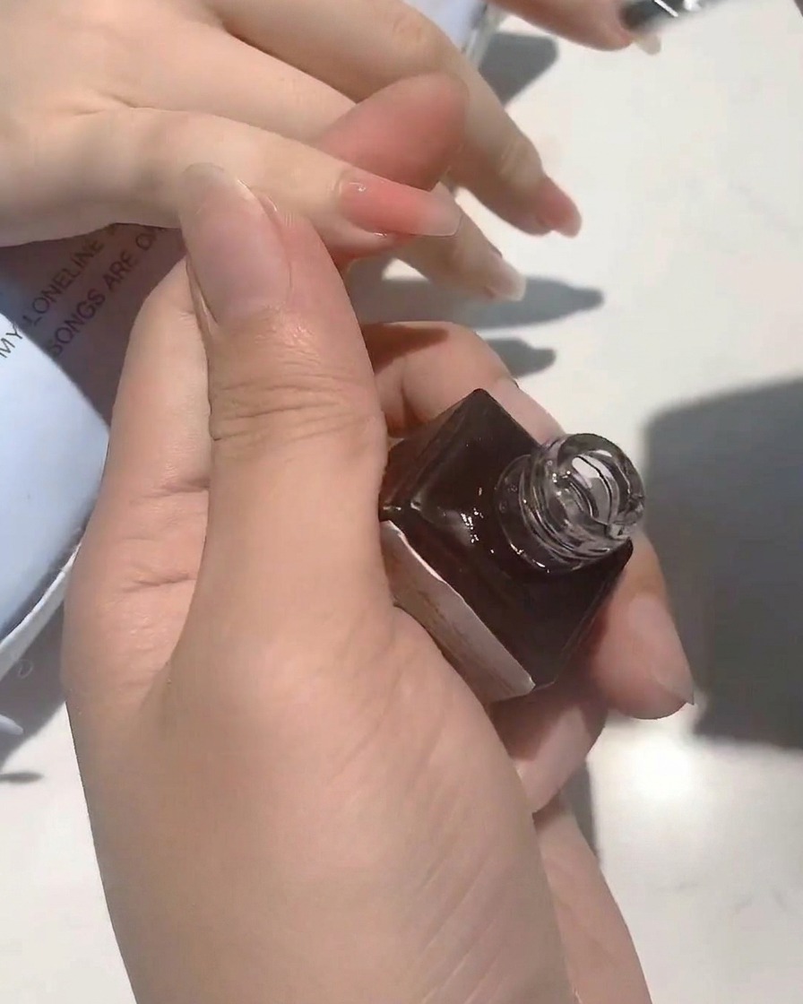 Gros plan dun pinceau appliquant un top coat transparent et brillant sur un ongle de couleur nude.