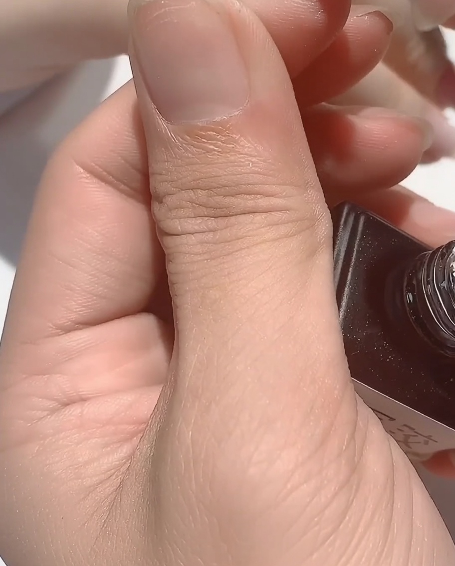 Un pinceau appliquant une rubber base transparente et épaisse sur un ongle aux reflets irisés.