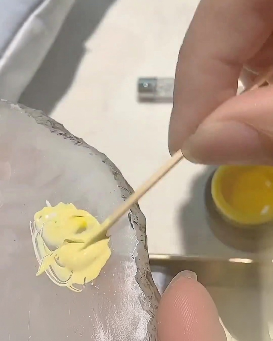 Une petite goutte de gel rouge ajoutée au mélange de gel jaune sur une palette.