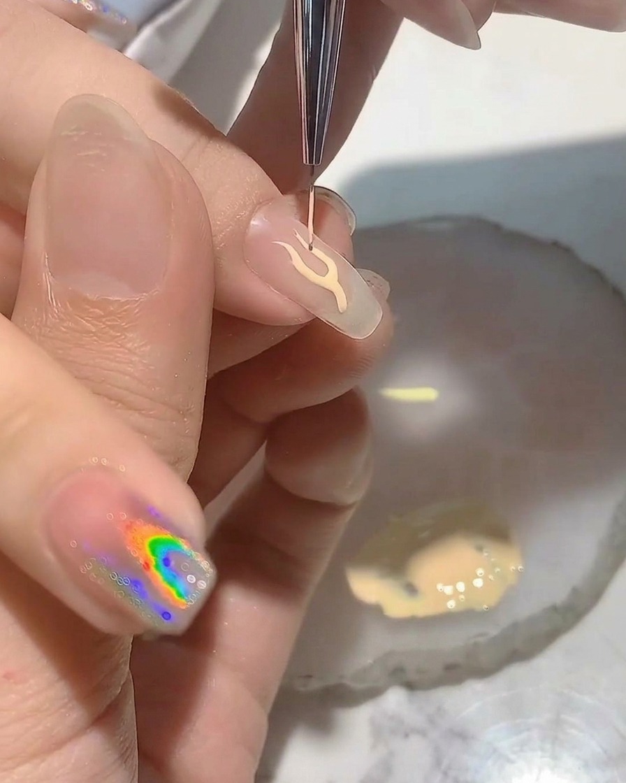 Une prothésiste ongulaire utilisant un pinceau liner fin pour dessiner le contour délicat dune flamme sur une capsule transparente.