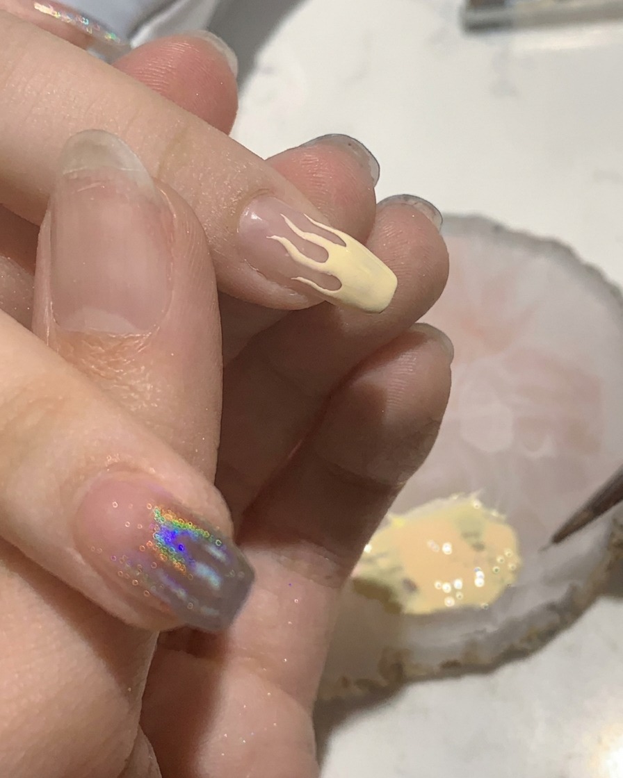 Un petit pinceau plat remplissant de couleur pêche un motif de flamme sur un ongle manucuré.
