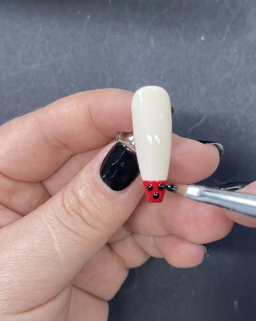 Un pinceau liner fin appliquant une bande horizontale de vernis gel rouge juste au-dessus de la pointe noire sur longle.