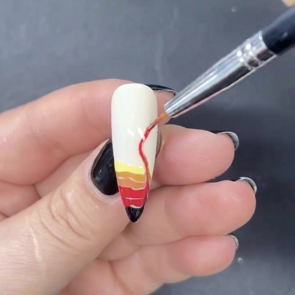 Un pinceau liner fin utilisé pour étirer les bandes horizontales de gel coloré vers le haut en formes de flammes en S.