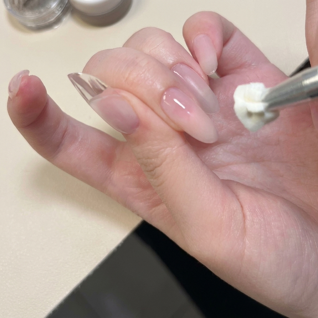 Gros plan dun outil métallique appliquant et tapotant du gel solide blanc sur le bord dun ongle naturel.