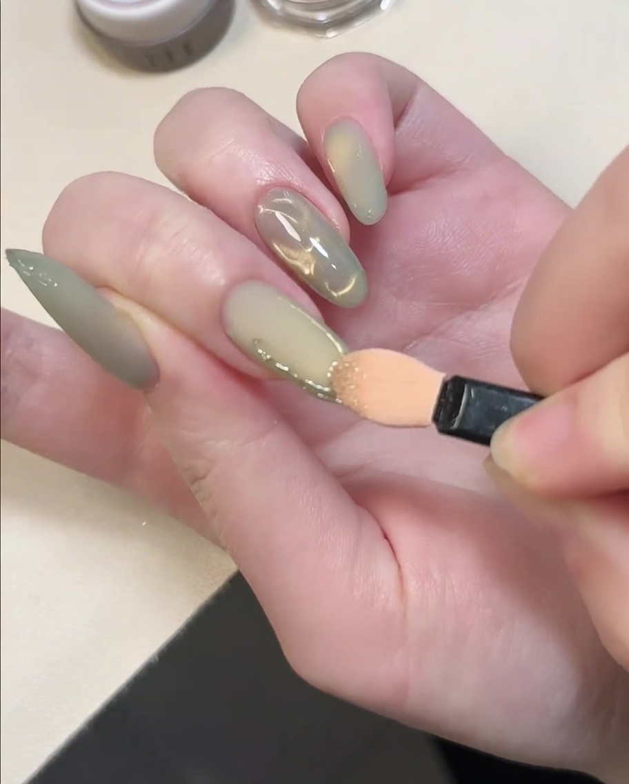 Un embout applicateur de fard à paupières frottant de la poudre chrome dorée sur des lignes en gel 3D sur un ongle.