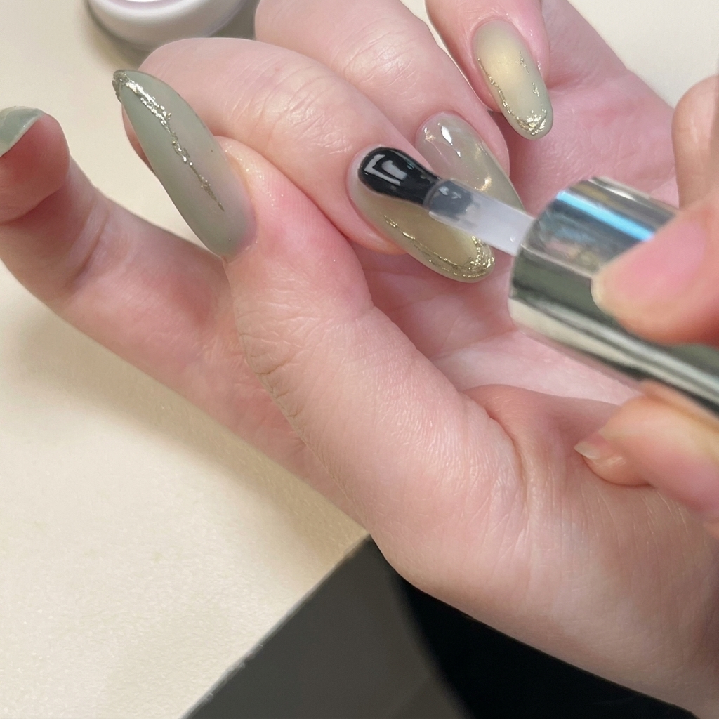 Un pinceau appliquant avec précision une couche de gel de renfort transparent sur les lignes 3D dorées dun ongle.
