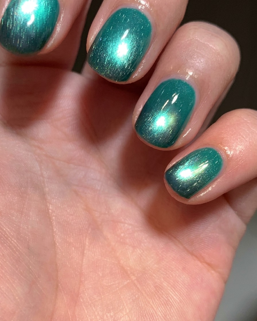 Un pinceau appliquant une couche de vernis gel œil-de-chat vert lac brillant sur un ongle ayant une pointe noire.