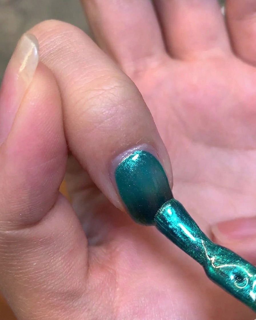 Un aimant en métal tenu près du côté de longle pour manipuler le gel vert en un reflet œil-de-chat.