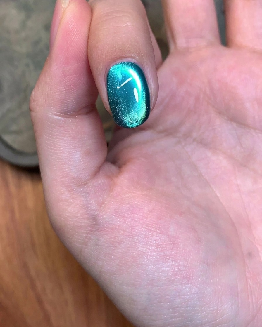 Un outil magnétique utilisé dans un mouvement circulaire sur un ongle peint en gel vert pour ajuster le reflet.