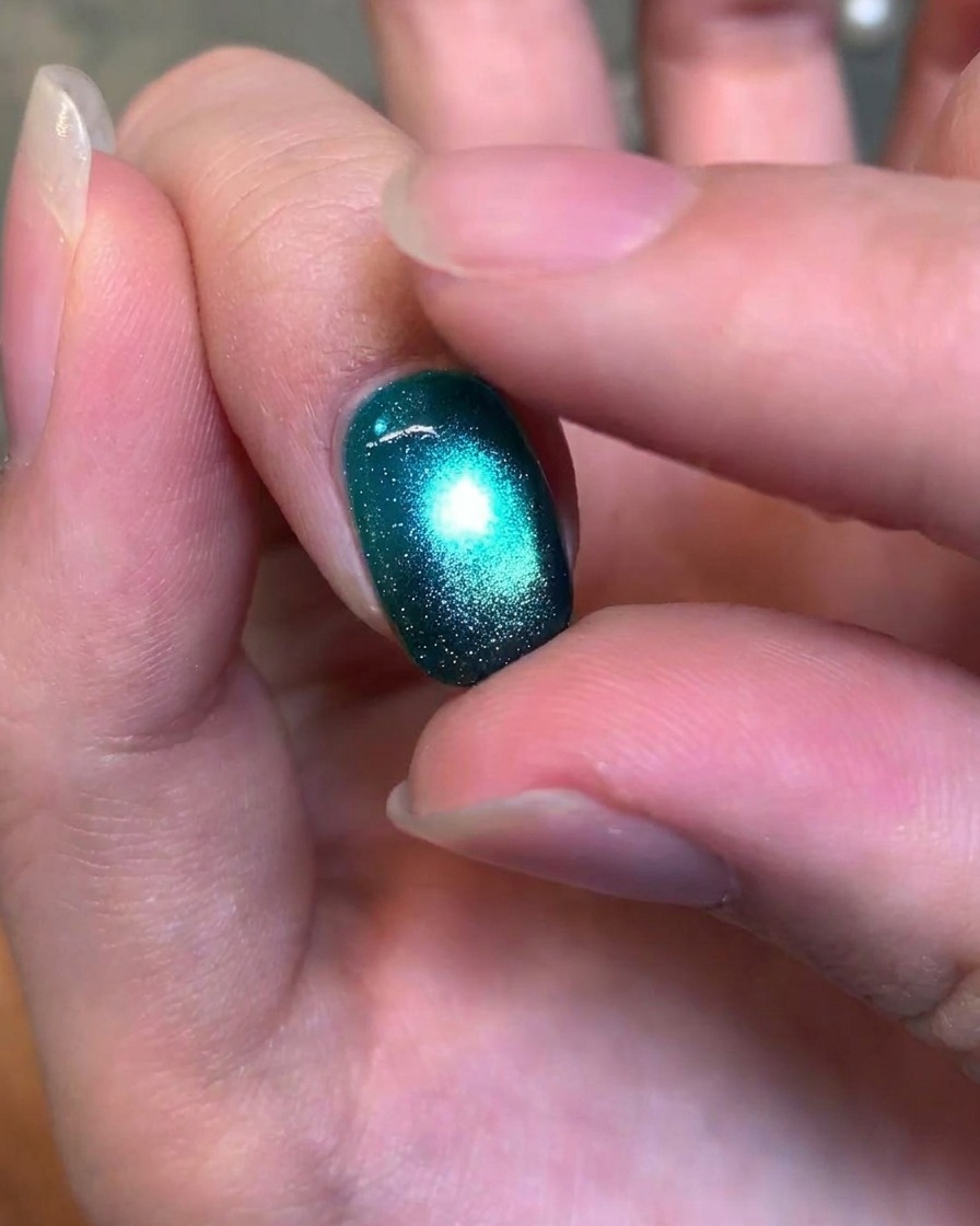 Gros plan dun doigt testant délicatement la texture dun ongle en gel œil-de-chat vert foncé, brillant et fini.