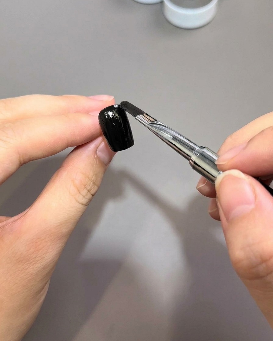 Un pinceau à ongle applique une couche lisse de vernis gel noir sur une surface dongle préparée.