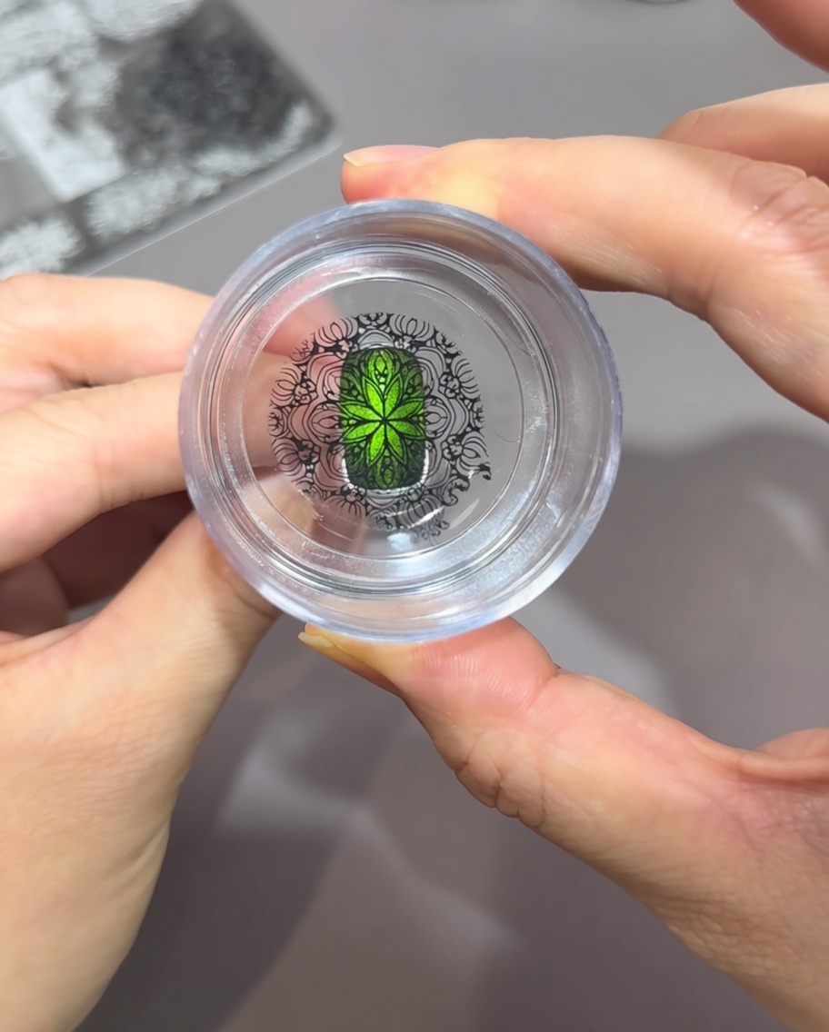 Vue à travers un tampon en silicone transparent, montrant un motif noir complexe aligné sur un ongle vert oeil de chat.