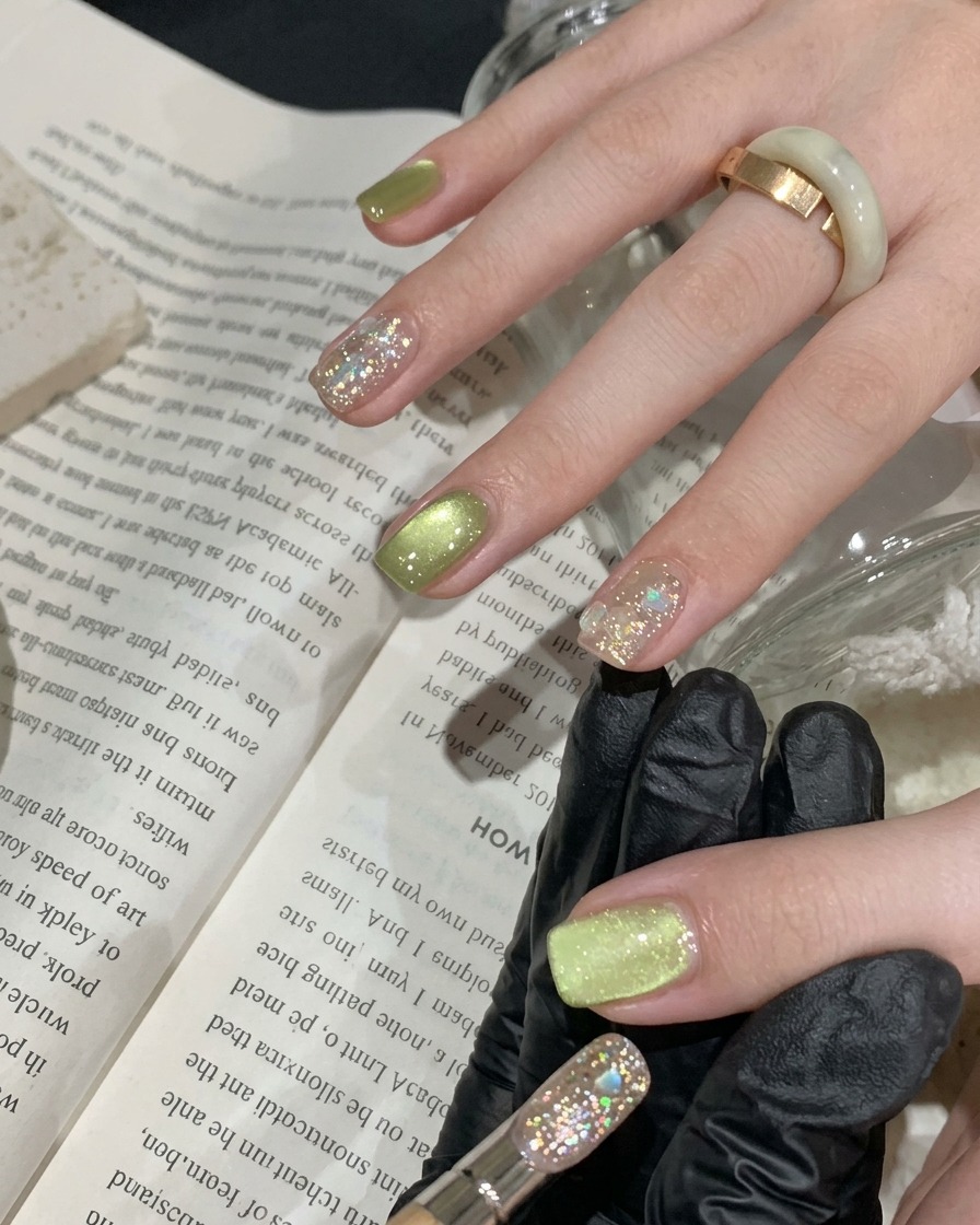 Un pinceau appliquant une fine couche de vernis gel œil de chat vert sur un ongle naturel.