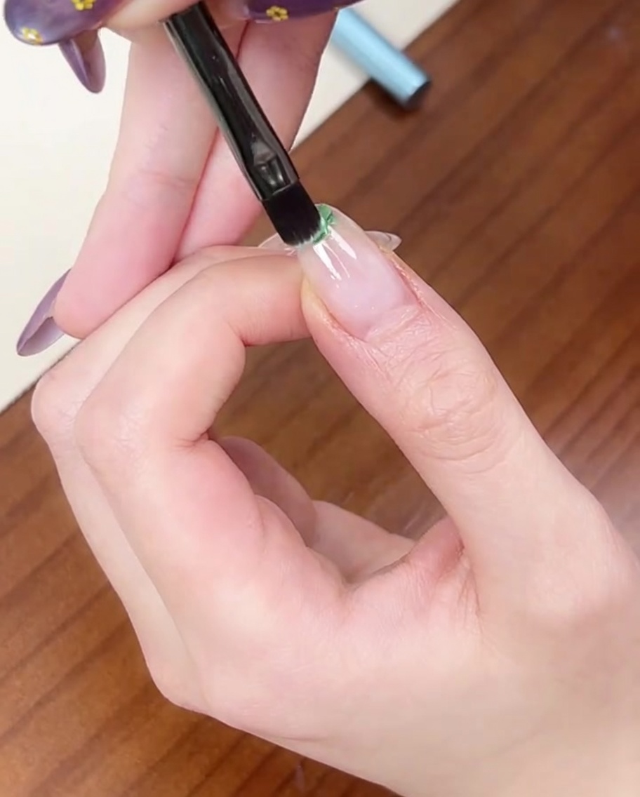 Un pinceau plat applique une petite touche de vernis gel vert clair sur le bord libre dun ongle naturel.