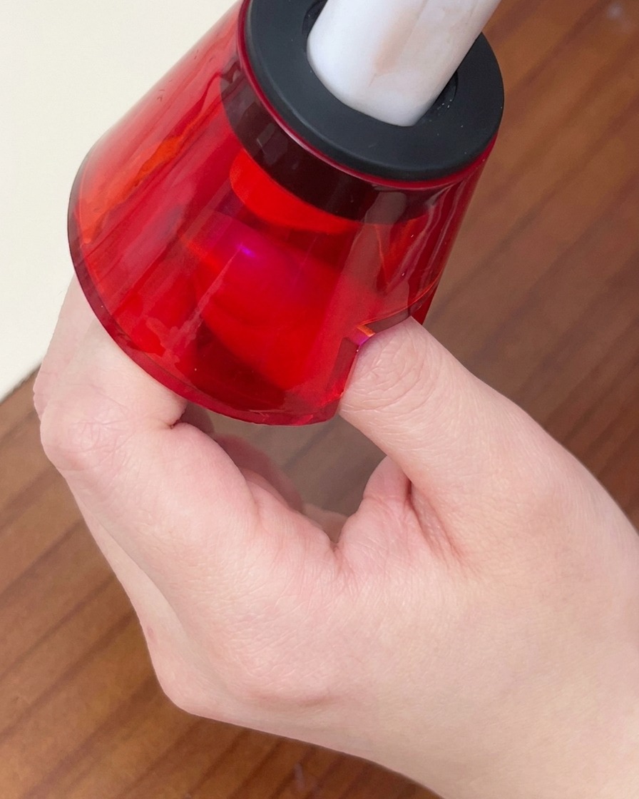 Un doigt placé sous une petite lampe LED portable rouge pour catalyser le vernis gel.