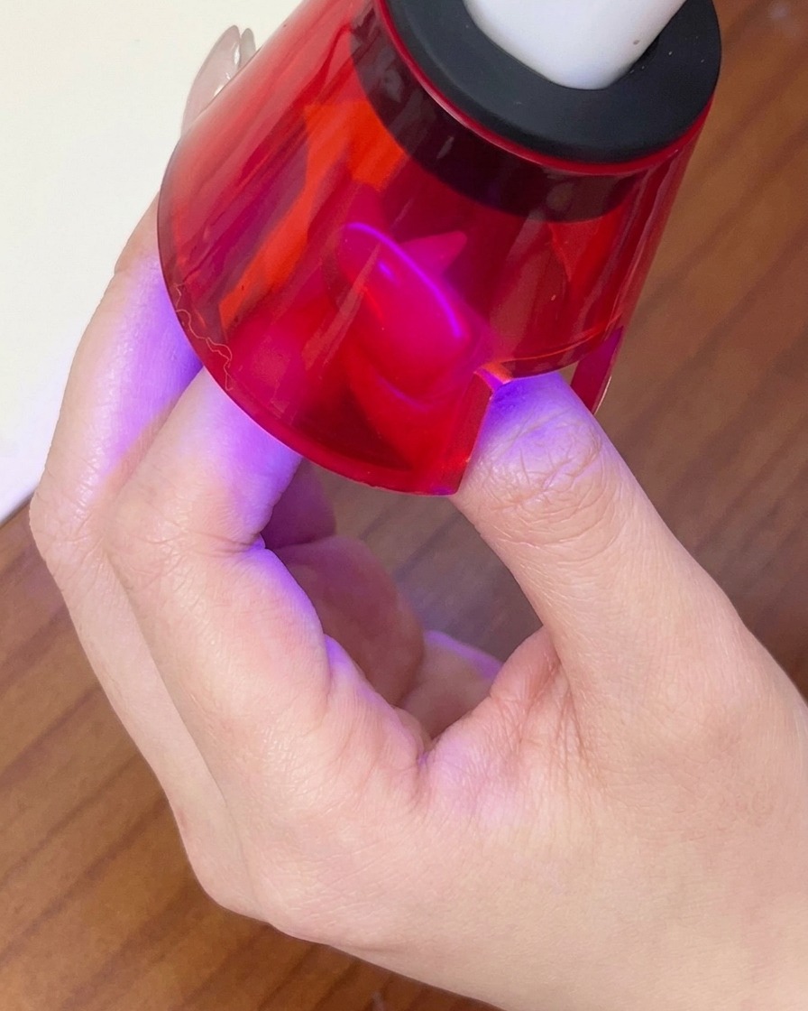 Un doigt catalysant sous une lampe LED portable rouge pour fixer le motif du gel magnétique.