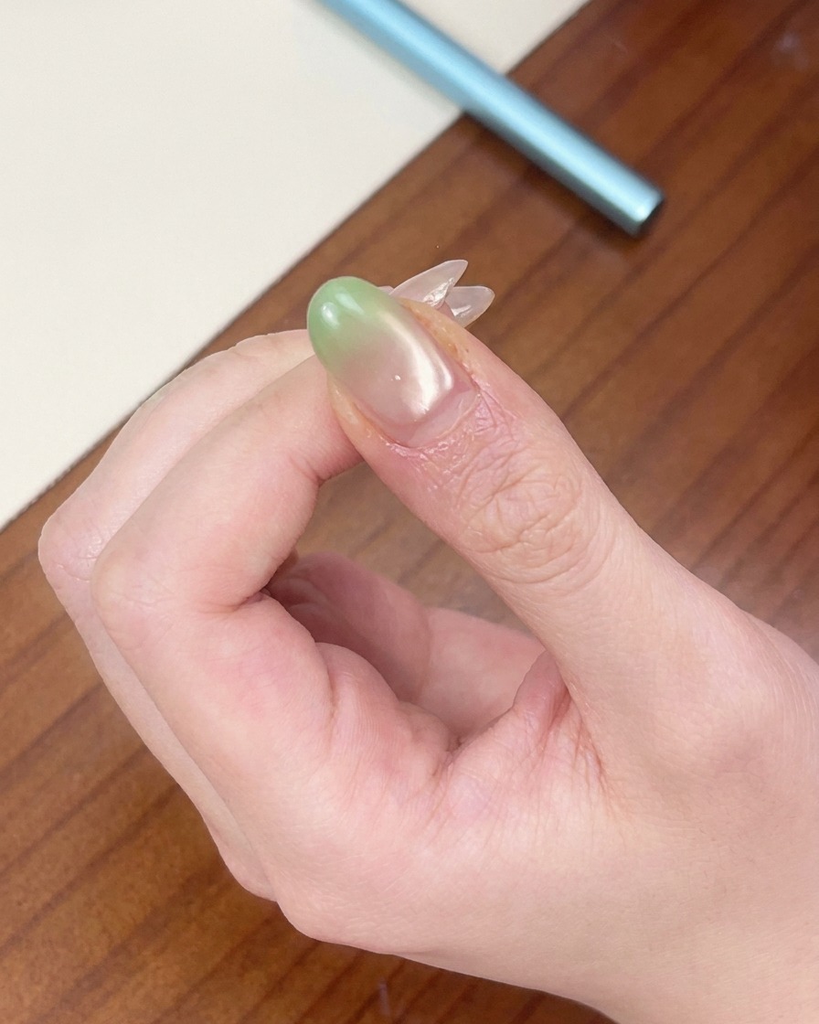Un ongle avec un dégradé vert positionné sous une mini lampe UV portable rouge.