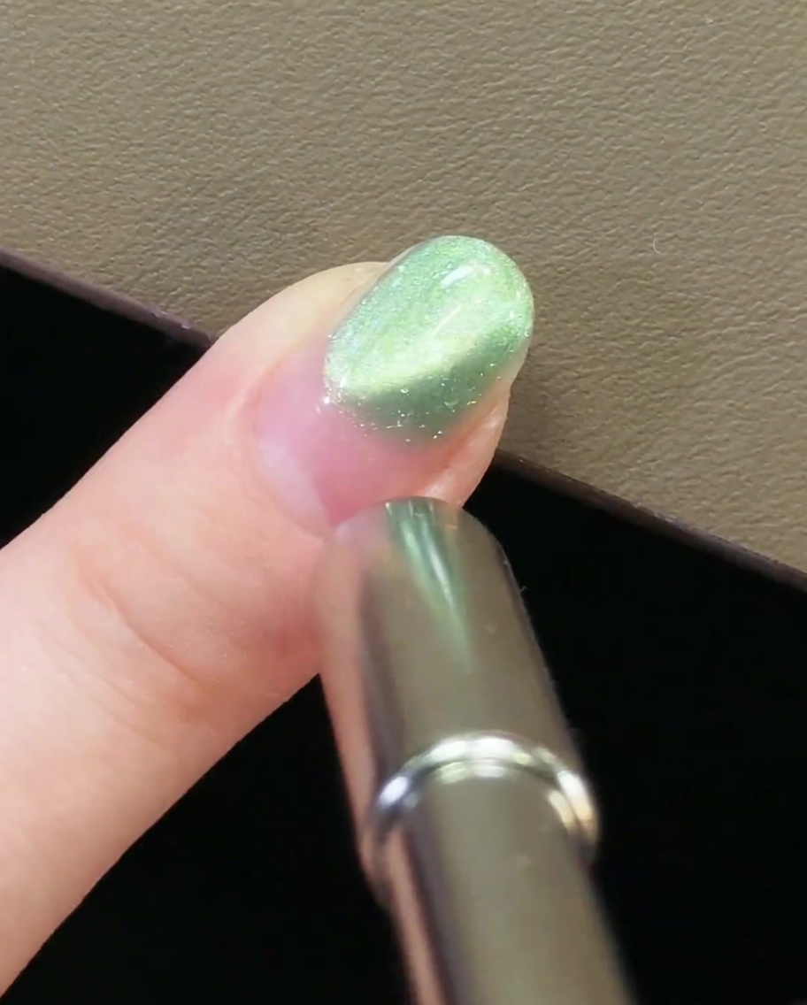 Un aimant métallique positionné au niveau de la cuticule sur un ongle avec du gel magnétique cat-eye vert.