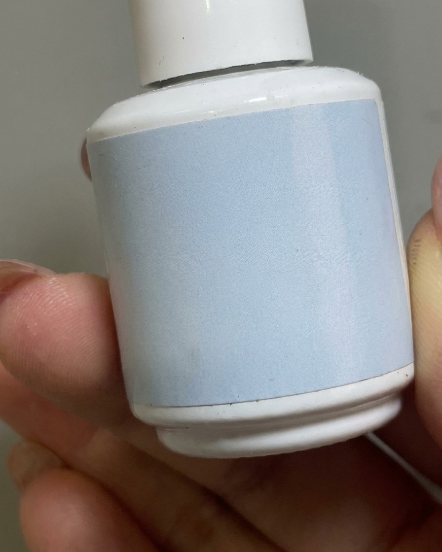 Un pinceau appliquant un top coat mat transparent sur la base gel nude dun ongle.