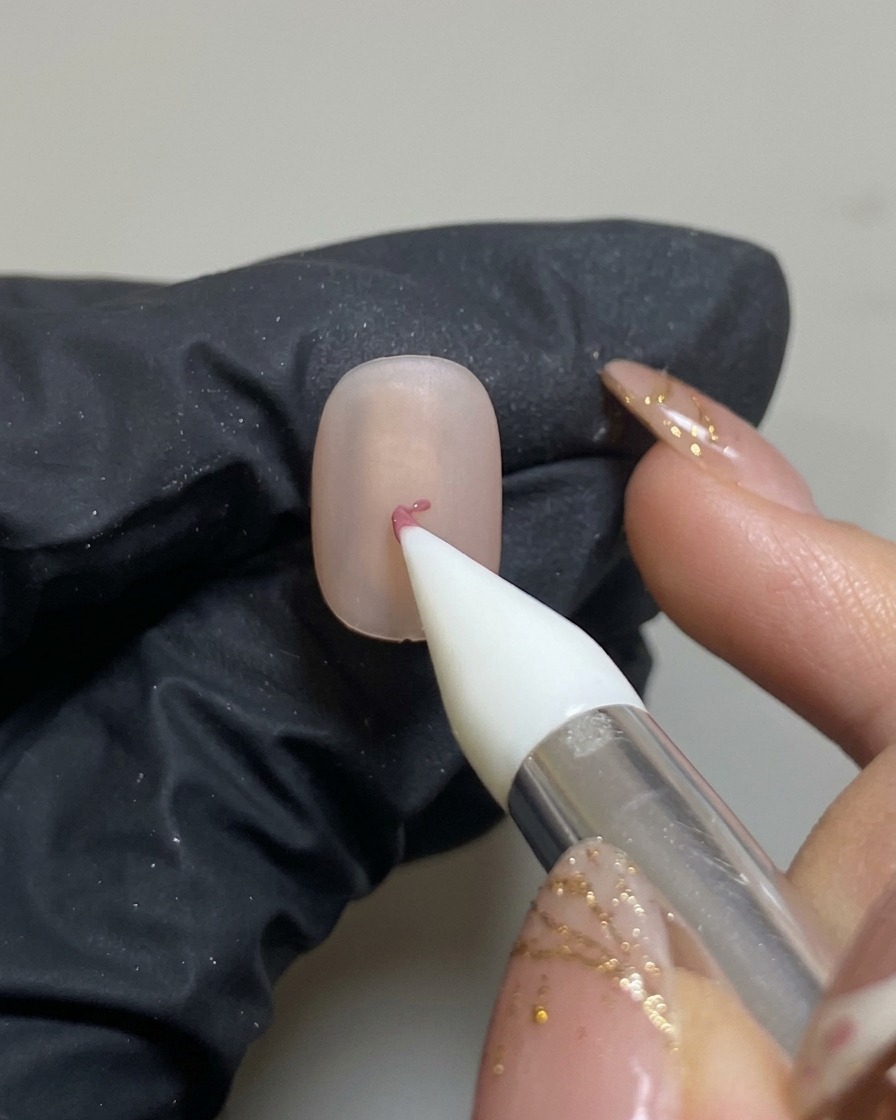 Un outil silicone déposant un petit point de gel rose au centre dun ongle nude au fini mat.
