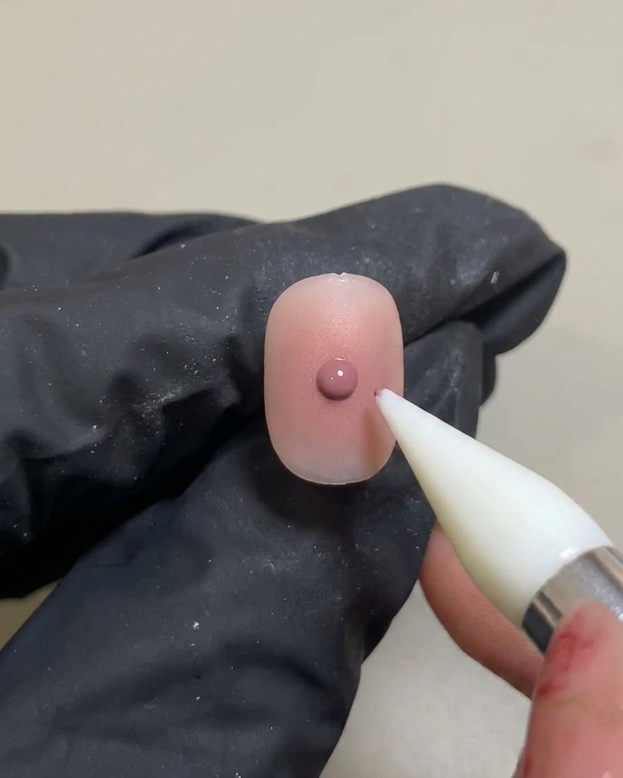 Un outil silicone appliquant un petit point concentré de gel rose sur un dégradé blush préalablement catalysé.