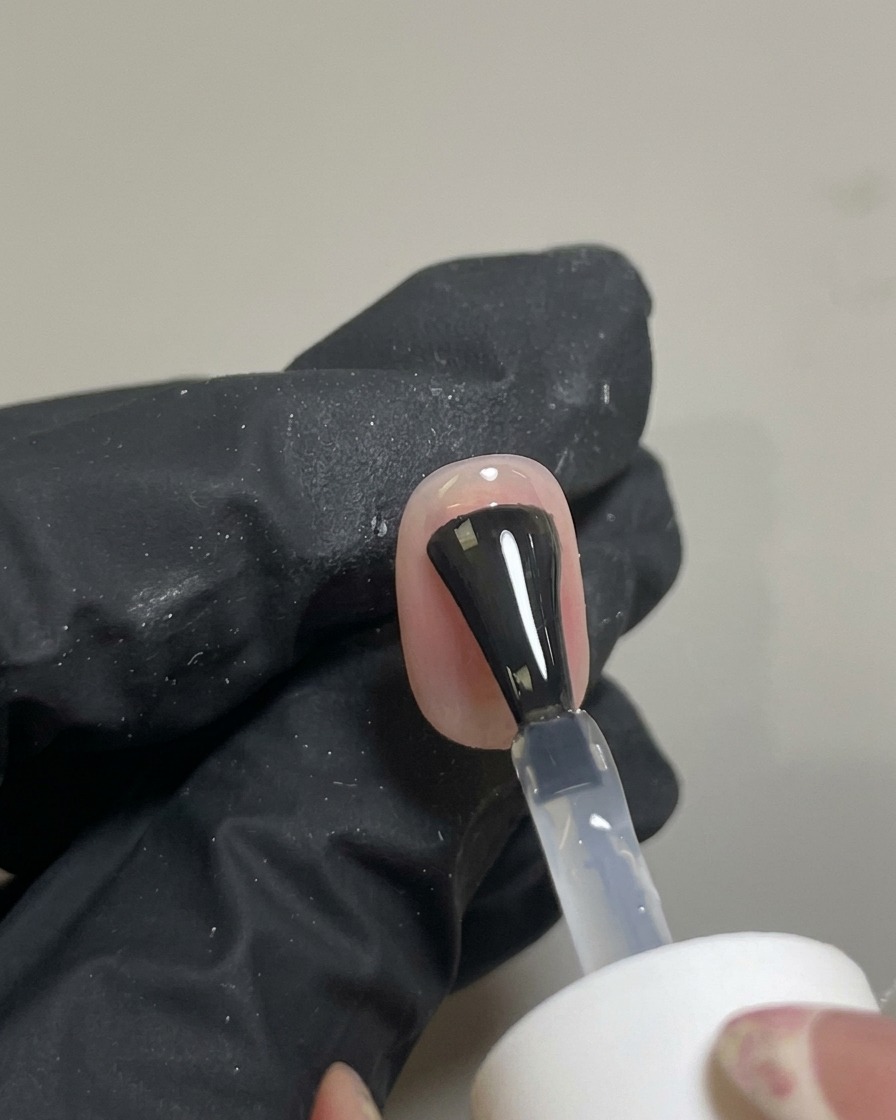 Un pinceau appliquant un top coat brillant transparent sur le nail art blush terminé.
