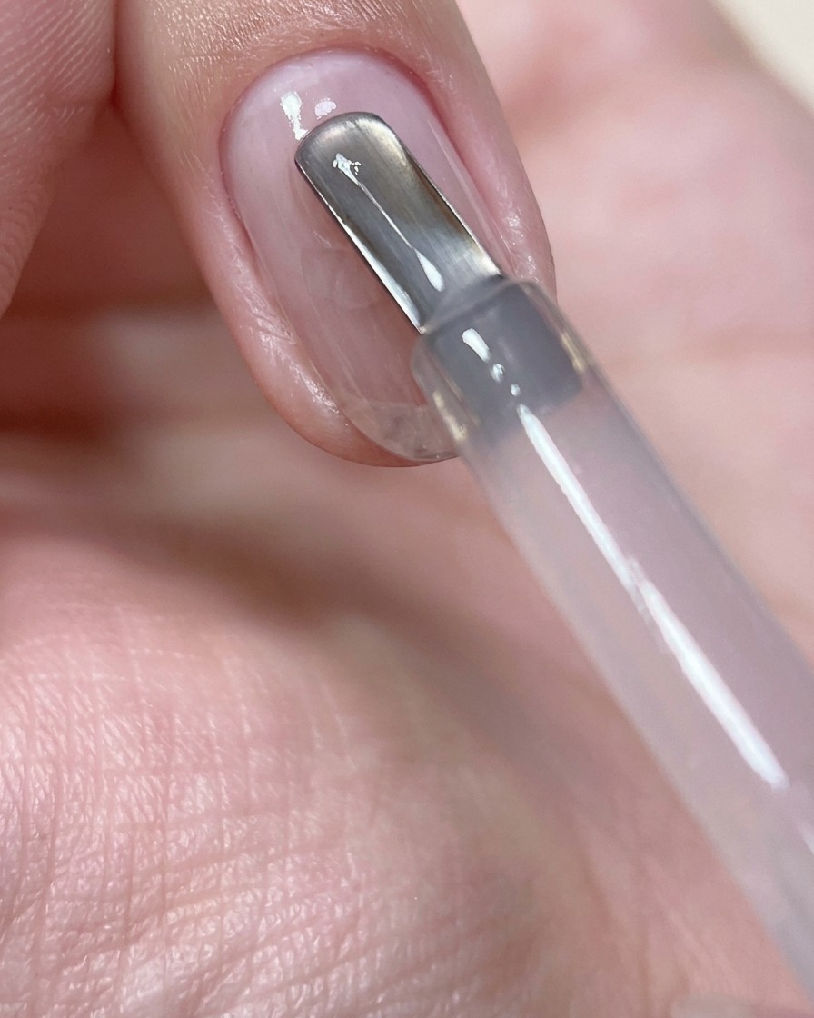 Gros plan sur un pinceau à ongles appliquant une perle de gel de construction rose transparent au centre de longle.