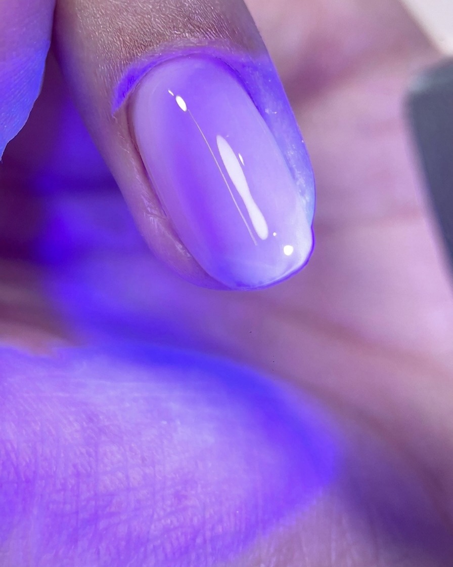 Un ongle avec une couche de gel rose brillant non catalysé sous la lumière violette dune lampe de manucure.