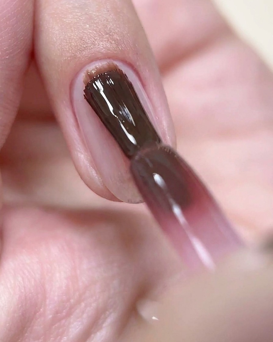 Un pinceau appliquant une fine couche de gel vernis rose vin profond sur un ongle préparé.