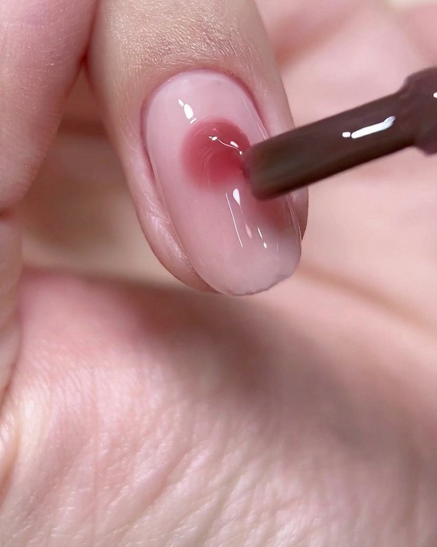 Un pinceau déposant une perle ronde et précise de gel rose vin au centre dune base dongle rose clair.