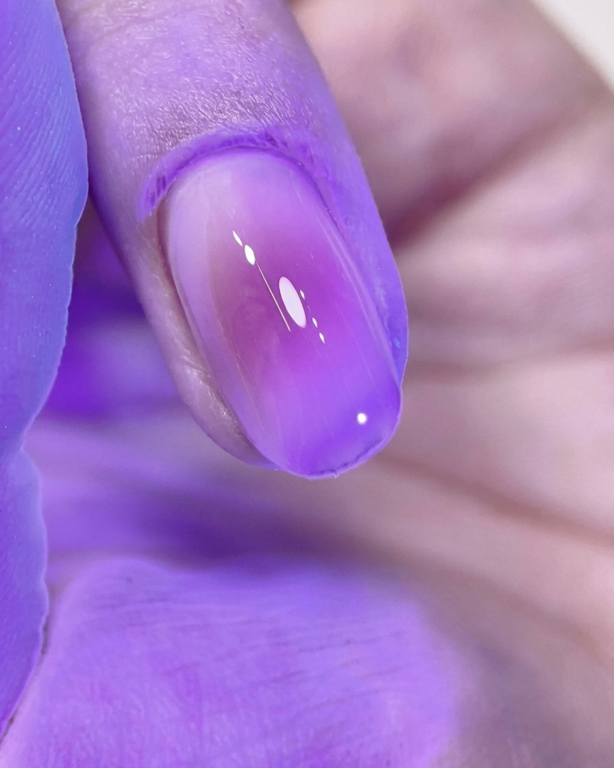Un ongle blush rose parfaitement manucuré en cours de catalyse sous la lumière violette dune lampe UV/LED.