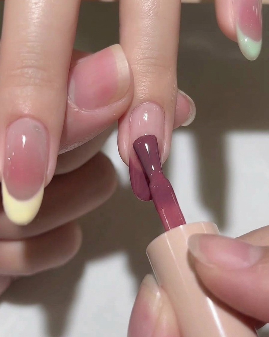 Un pinceau estompant une goutte de gel rose sur un ongle pour créer un effet diffus.