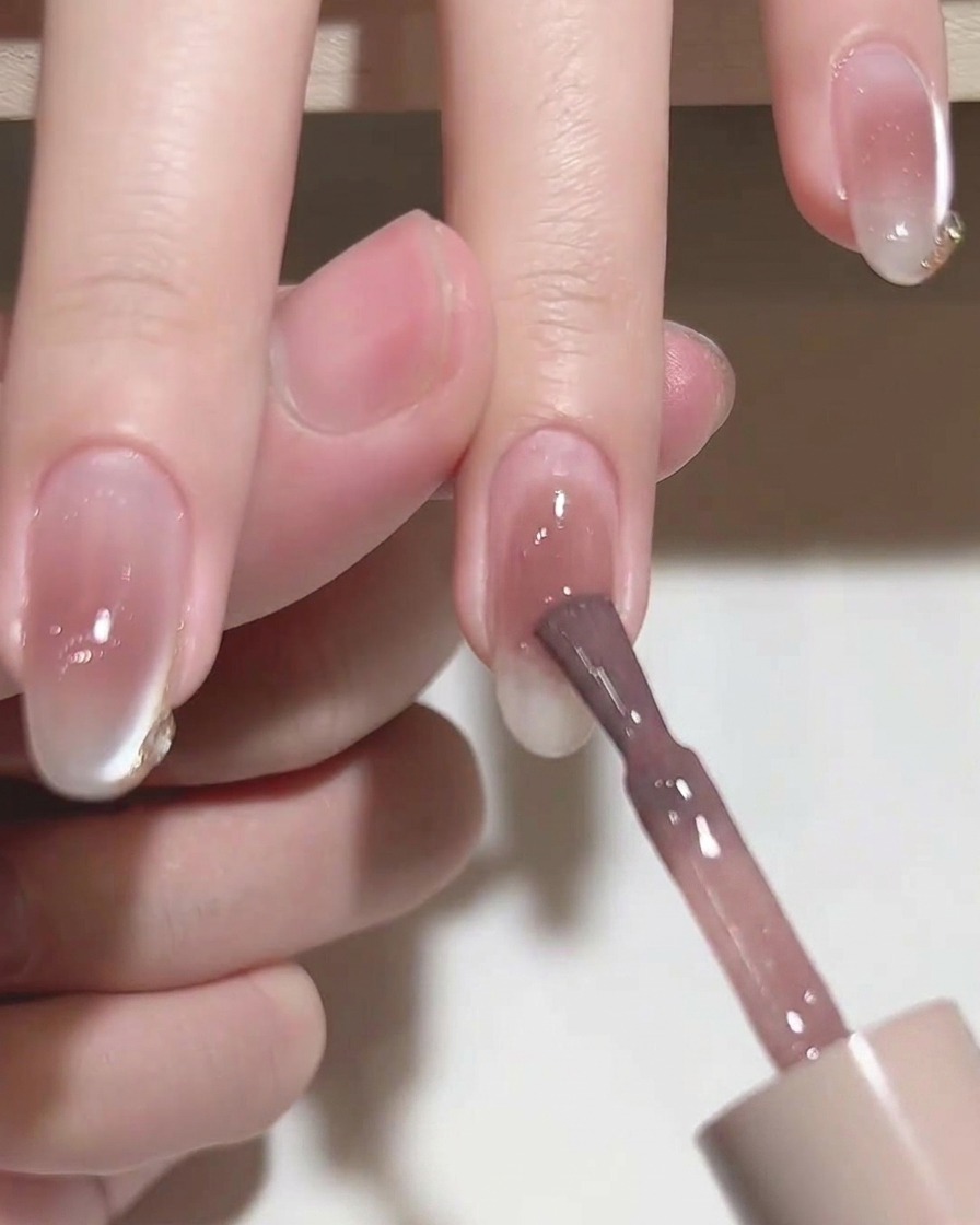 Un pinceau plat lissant le vernis gel rose sur un ongle.