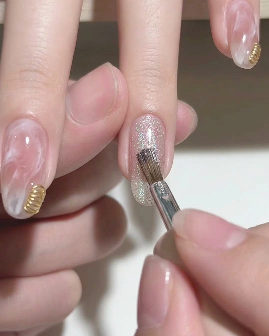 Un pinceau appliquant un vernis gel cat-eye argenté étincelant sur le bout dun ongle rose.