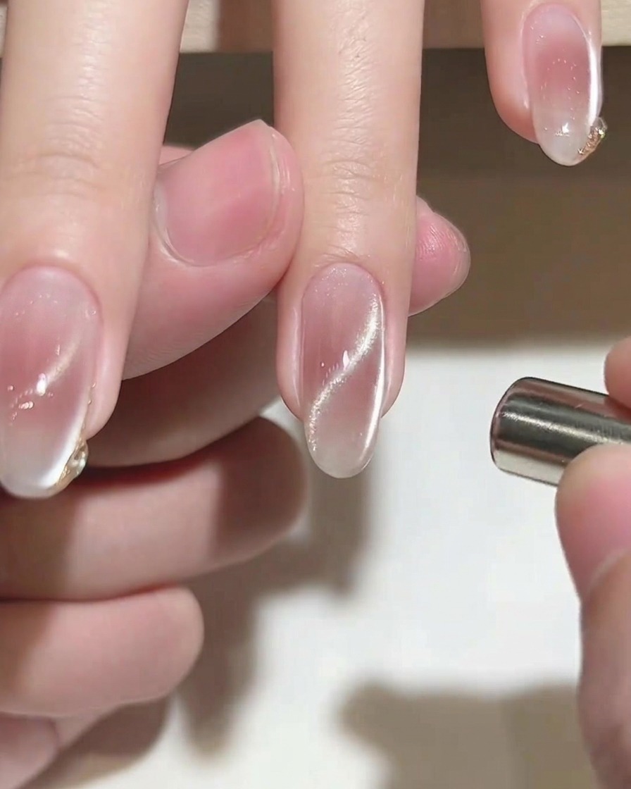 Un pinceau liner fin ajoutant un détail doré délicat sur le bout dun ongle rose.