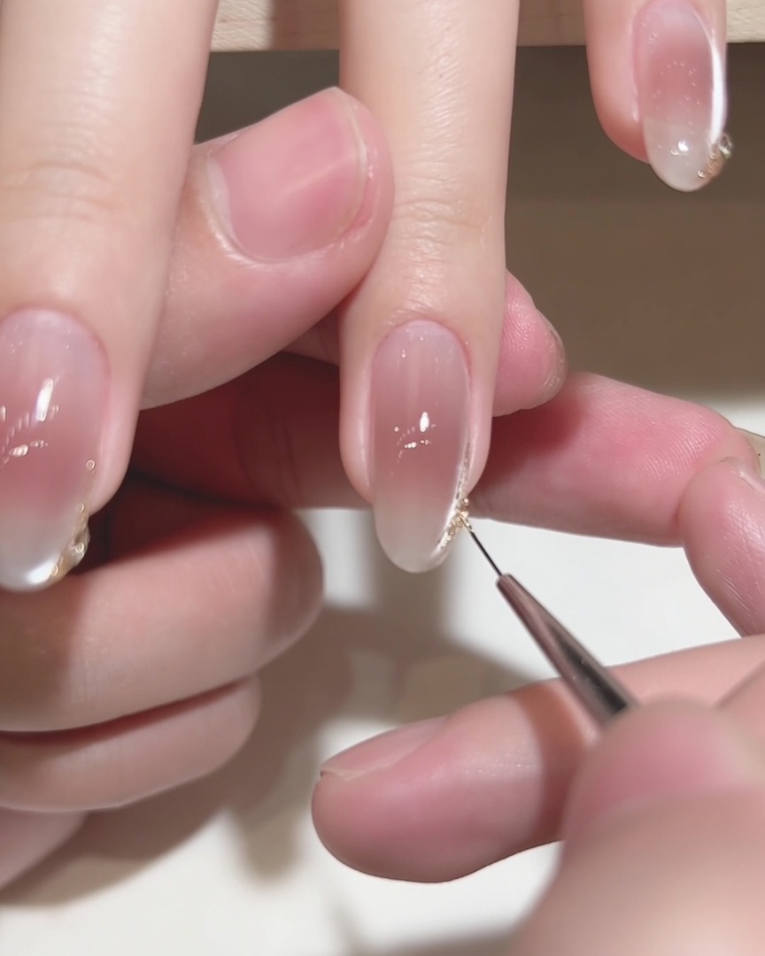 Gros plan dun pinceau liner fin appliquant des détails dorés sur le bout dun ongle manucuré.