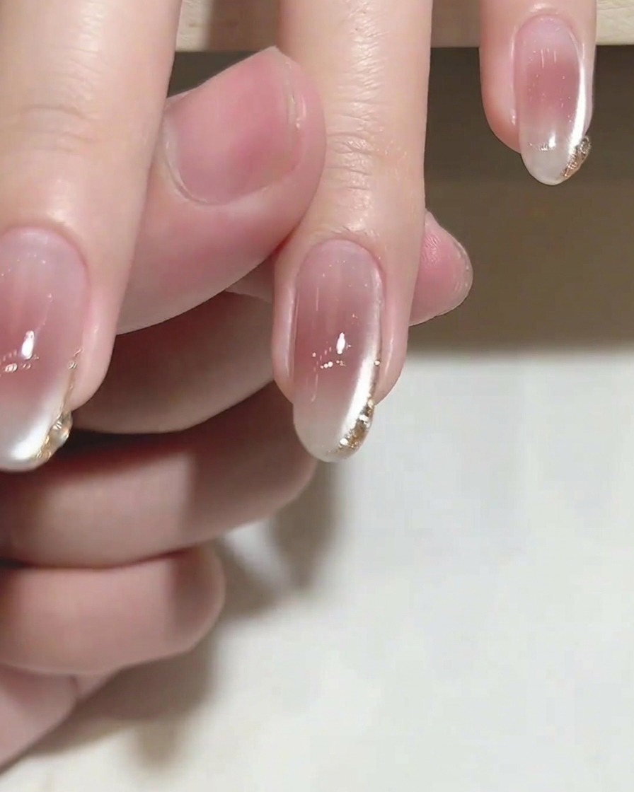 Un pinceau appliquant un top coat transparent brillant sur un ongle présentant des détails dorés délicats.