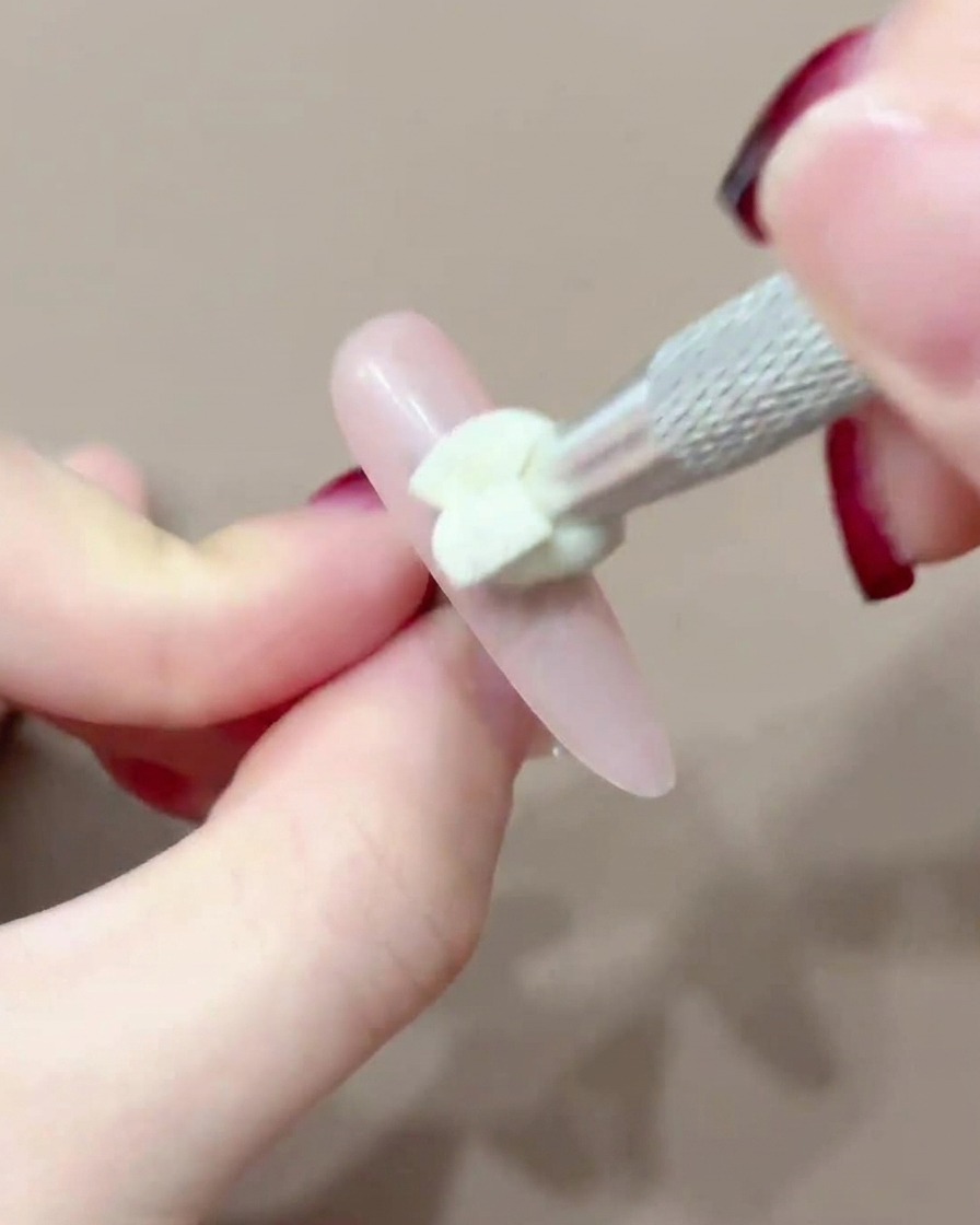 Un outil à embout en silicone tapotant du pigment rose au centre dun ongle.
