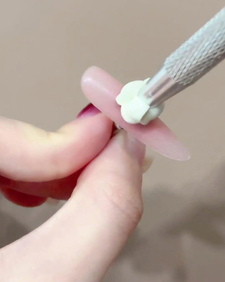 Un pinceau appliquant un petit point précis de gel blush rose au centre dun ongle.