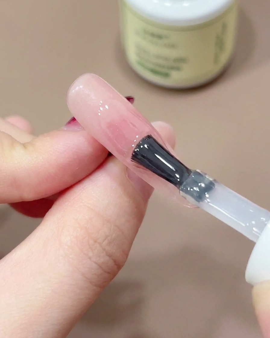 Un pinceau à ongles appliquant un top coat transparent et brillant sur un design dongle blush rose.