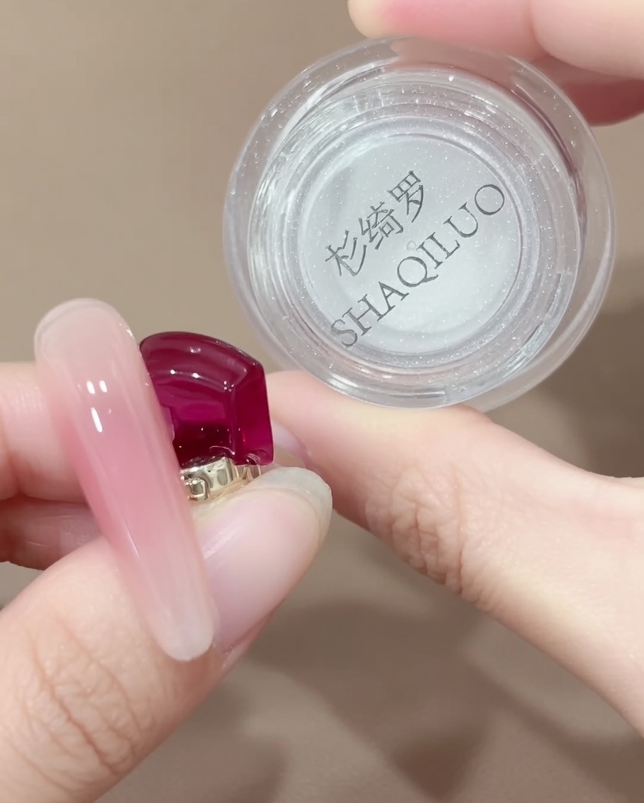 Un stylo applicateur à embout en silicone prélevant une petite quantité de poudre chromée iridescente dans un pot.