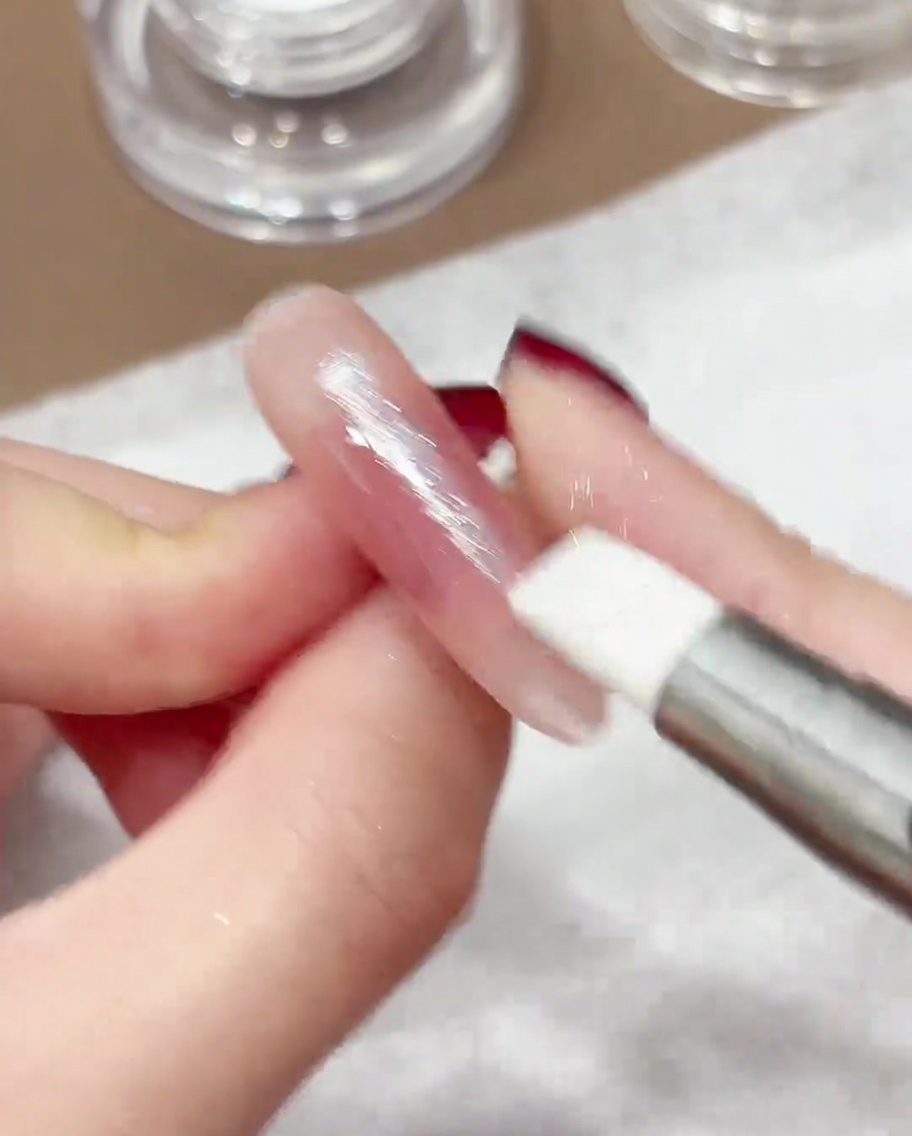 Un stylo en silicone lustrant la poudre chromée iridescente sur la surface dun ongle manucuré.