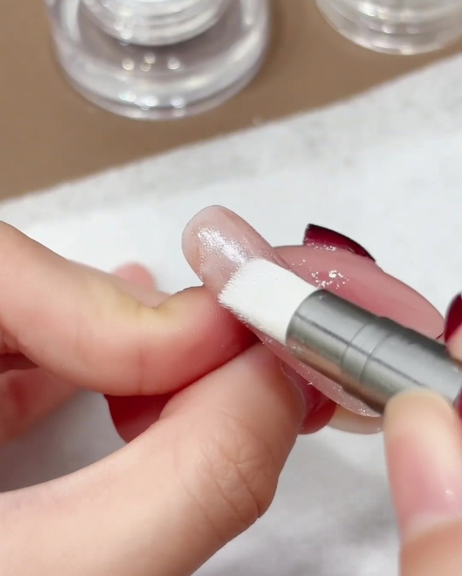 Gros plan dun stylo applicateur à embout en silicone lustrant la poudre chromée aurora iridescente sur la surface dun ongle.