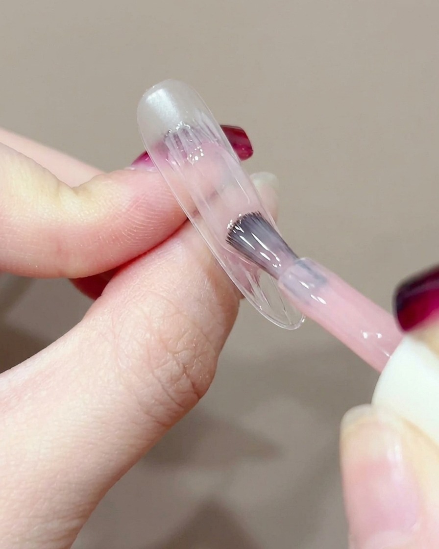 Gros plan sur un pinceau gel appliquant une petite touche de gel pêche au centre dun ongle nu.