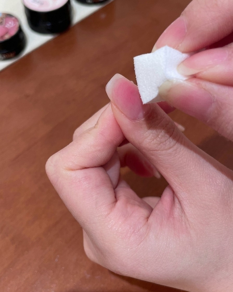 Une éponge à maquillage utilisée pour tapoter et estomper le gel pêche en un dégradé doux sur la surface de longle.
